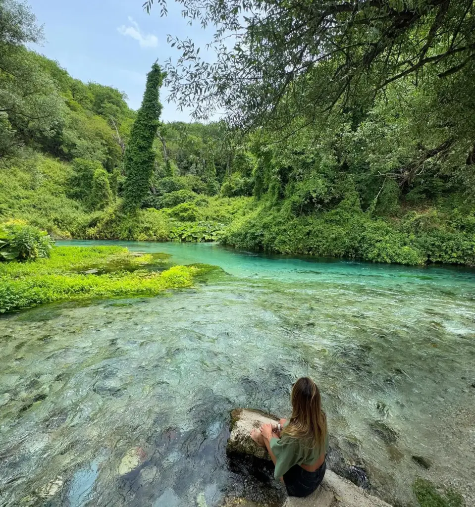 Woman sitting by the crystal-clear waters of Blue Eye Spring near Ksamil – a top natural attraction easily reached with a Ksamil car rental.