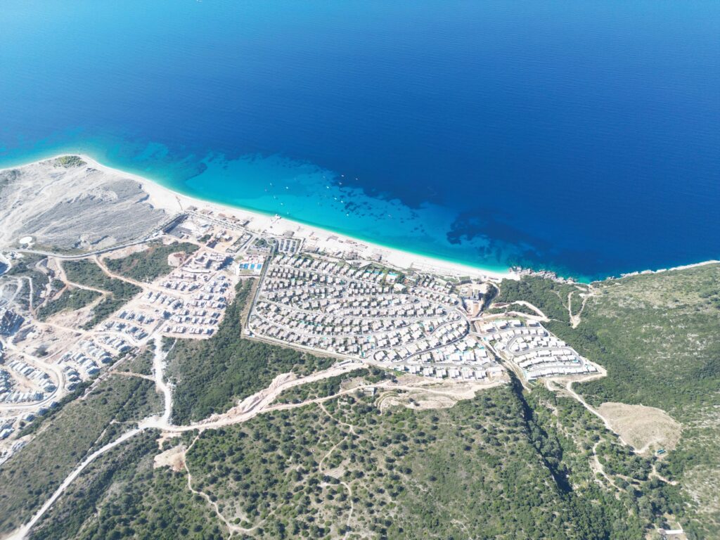Drone photo from Llogar Pass of resort development and turquoise coastline near Drymades Beach, Albanian Riviera.