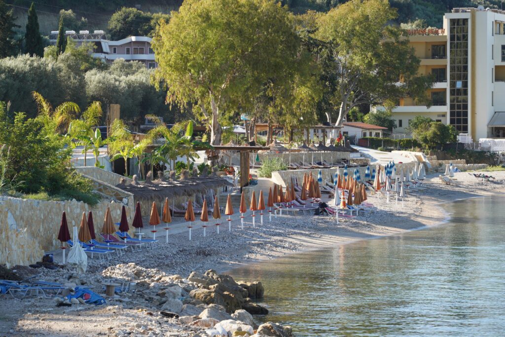 Pebble beach with colorful umbrellas and beachfront hotels in Radhime, Albania
