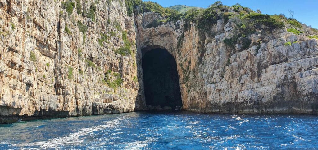 A sea cave entrance surrounded by steep limestone cliffs, viewed from a boat during a Vlora boat trip in Albania.